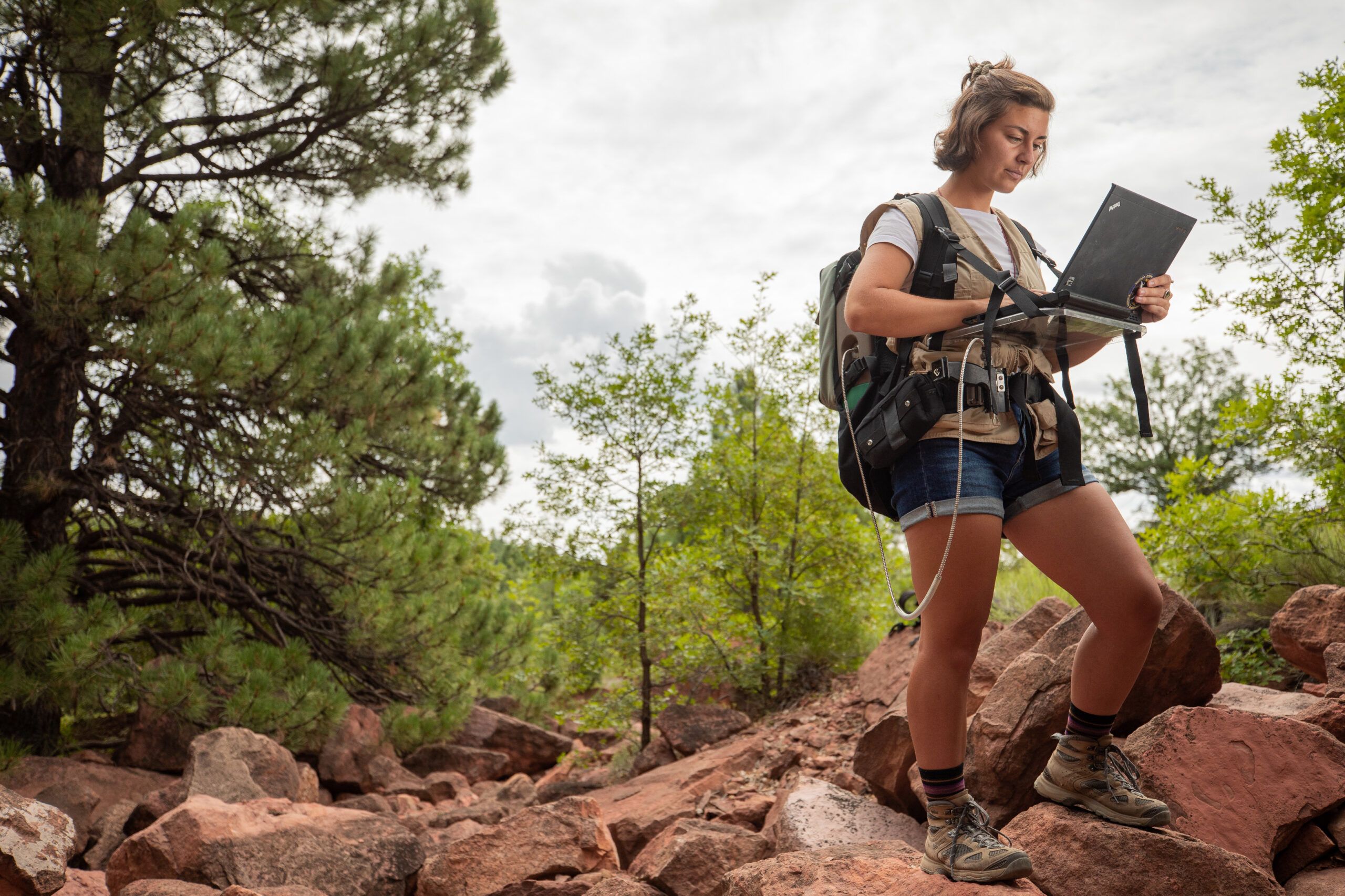 Student working on research in a red rock formation surrounded by trees.