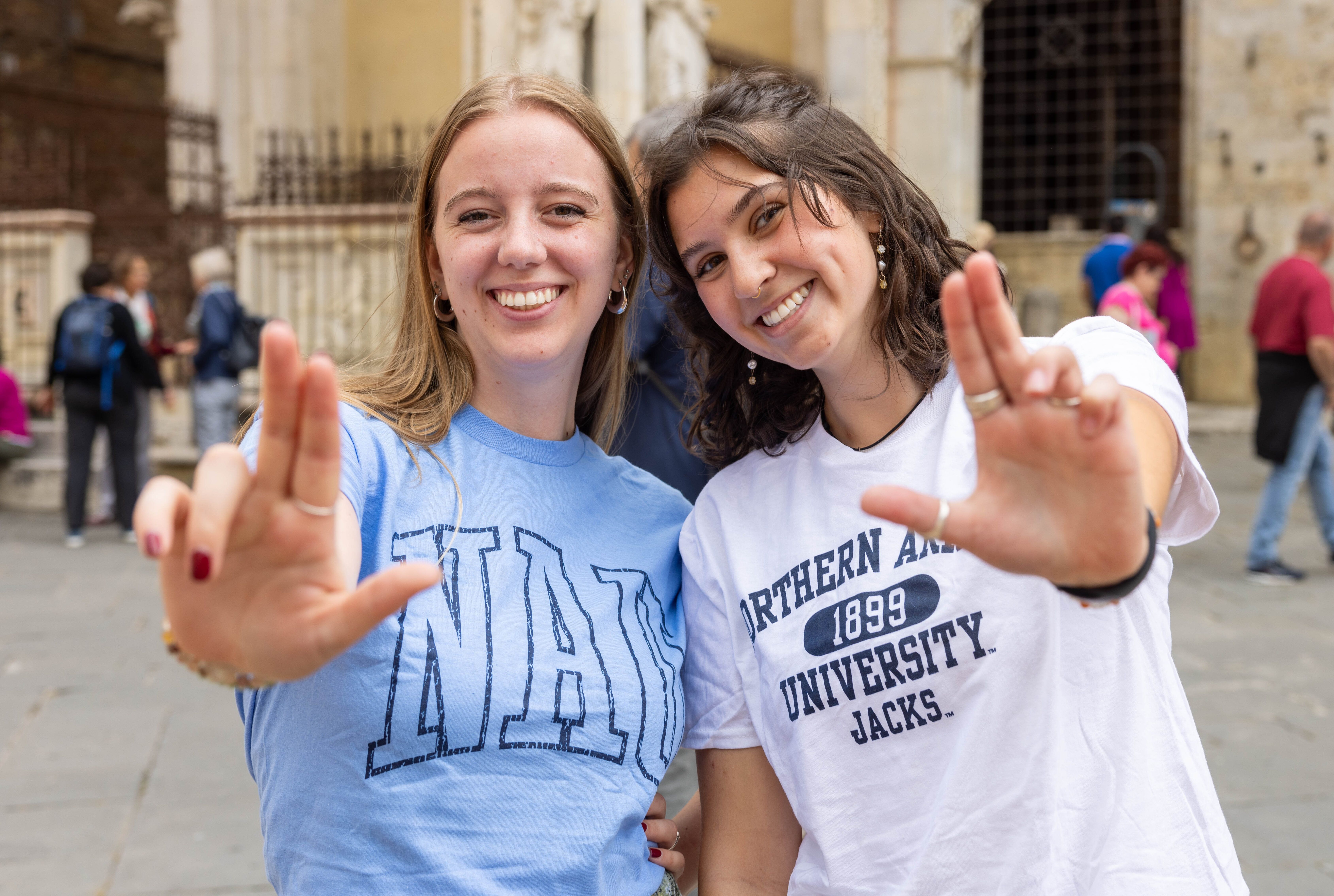 Two student are smiling for the camera and holding up the Jacks hand sign.