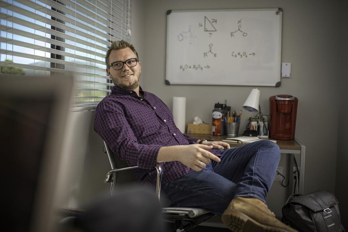A student sits in their dorm room with equations written on the whiteboard behind them.
