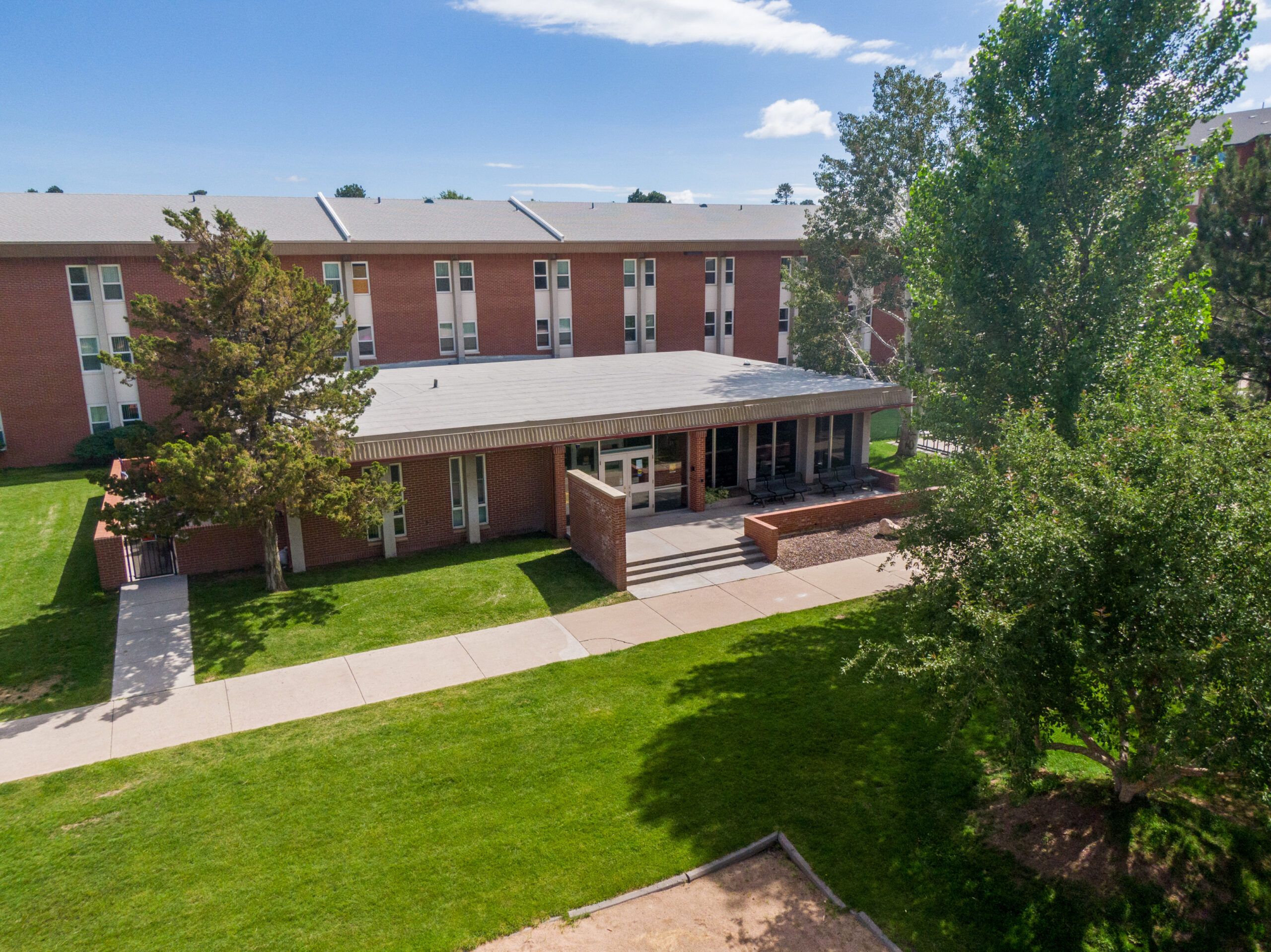 The exterior of Allen Hall, a residential living space, shaded by trees on a sunny day at NAU Flagstaff mountain campus.